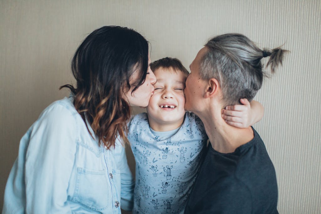 A joyful family moment with two parents kissing their smiling son indoors, symbolizing love.